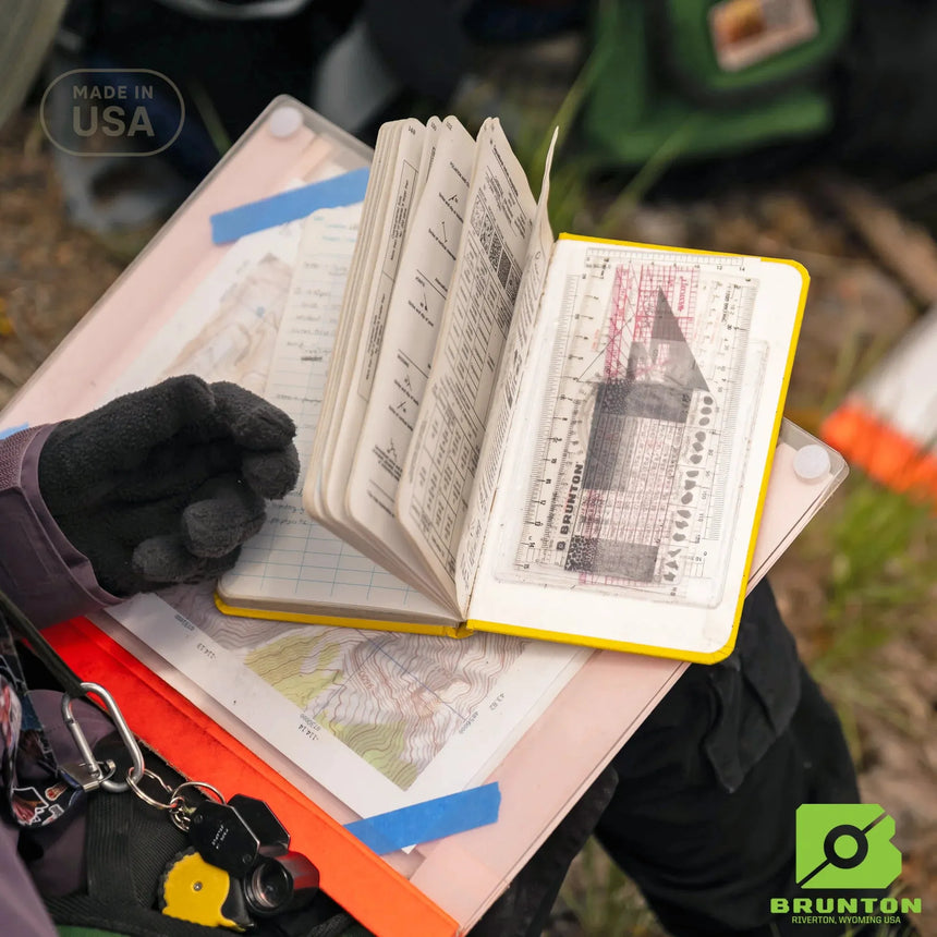 Open map book with maps and tools on a table outdoors, with Brunton logo visible.