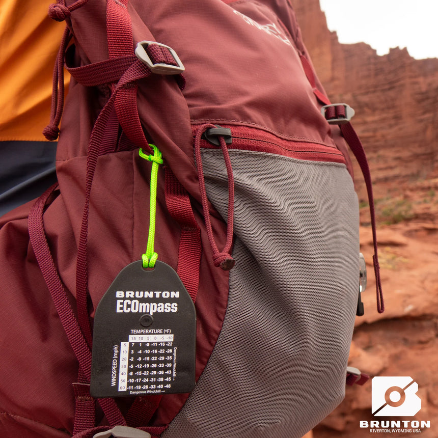 Person wearing a red backpack with a Brunton ECOpass temperature gauge tag in a desert setting.