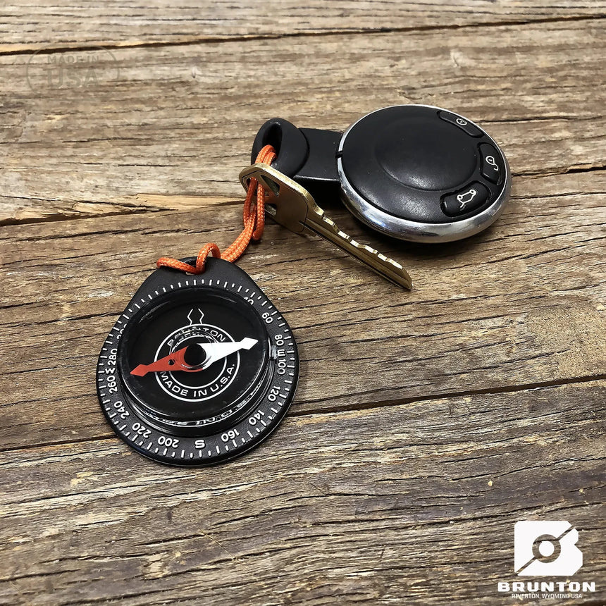 Compass and keychain with Brunton logo on a wooden surface
