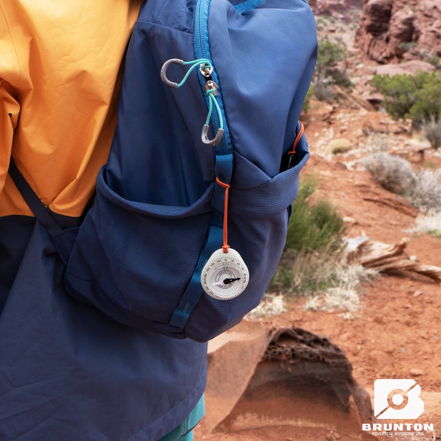 Person holding a blue backpack with a compass in a desert setting, featuring the Brunton brand.