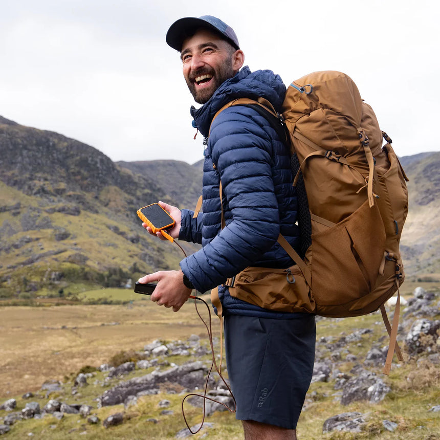 Man with a backpack using a device in a mountainous landscape