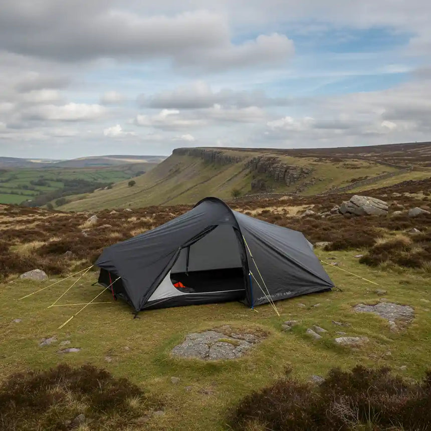 Tent pitched on a grassy hillside with a scenic view of rolling hills and a cloudy sky.
