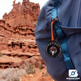 Blue backpack with a Brunton compass attached, set against a desert landscape.