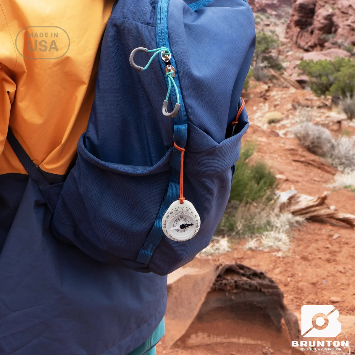 Person holding a blue backpack with a compass in a desert setting, featuring the Brunton brand.
