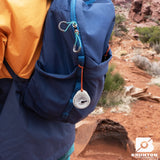 Person holding a blue backpack with a compass in a desert setting, featuring the Brunton brand.