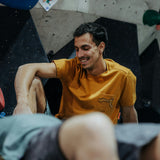 Wild Country Climbing Session Men's T-Shirt Joshua Brown - Model Sitting Down With Climbing Wall Background