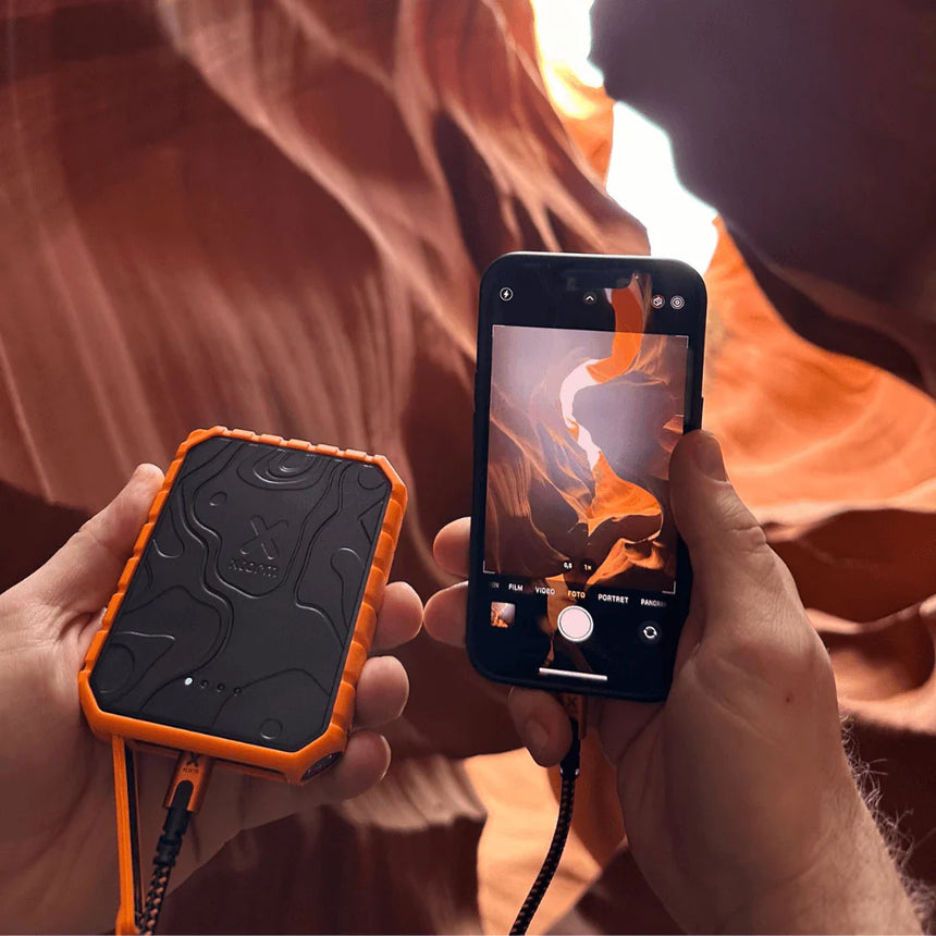 Person holding a phone with an orange and black case, taking a photo of a canyon.